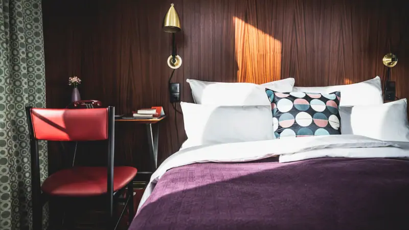 Zimmer & Suiten Bett mit Kissen und einem Schreibtisch davor im Hotelzimmer.