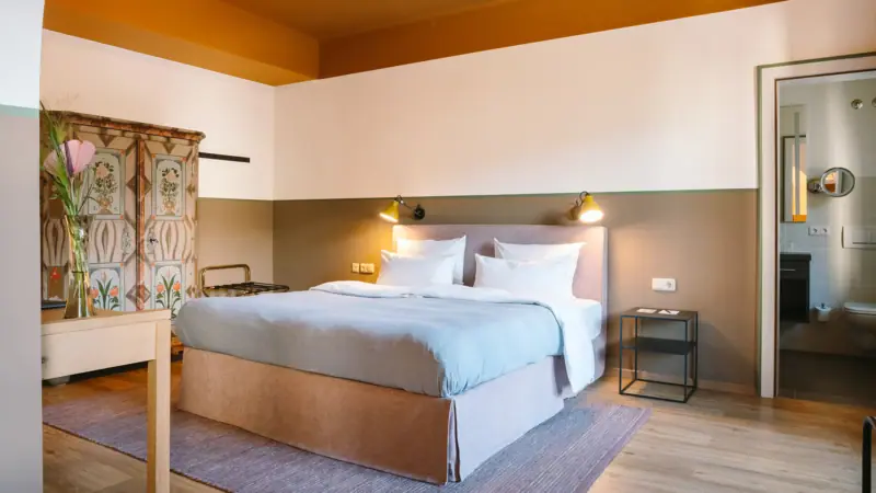 Ein Hotelzimmer im HENRI Garmisch-Partenkirchen mit einem großen gemütlichen bett, einem alten Schrank und einer Tür zum angrenzenden Badezimmer.