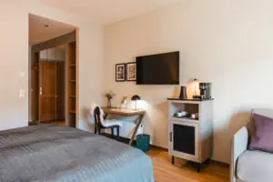 Schlafzimmer mit Bett, Schreibtisch und Fernseher.