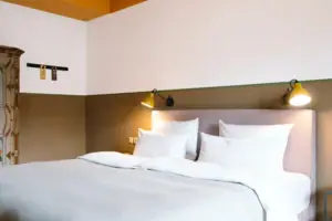 Ein gemütliches Bett in einem modernen Hotelzimmer im HENRI Hotel Garmisch-Partenkirchen.
