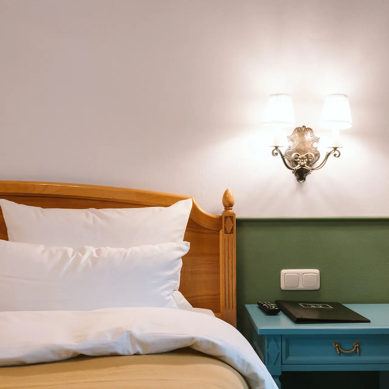 Hotelzimmer im HENRI Garmisch-Partenkirchen Ein Bett mit einem hölzernen Kopfteil vor einer grün-weißen Wand in einem stilvoll eingerichteten Hotelzimmer im HENRI Hotel Garmisch-Partenkirchen.
