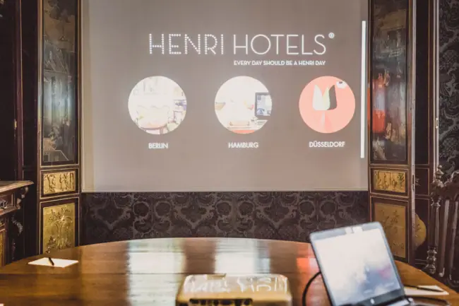 HENRI Berlin Präsentationsfläche Beamer auf einem Holztisch mit Leinwand davor