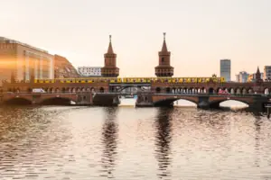 Ansicht der backsteingotischen Oberbaumbrücke in Berlin bei Sonnenuntergang mit einer gelben U-Bahn und Spiegelung im Wasser.