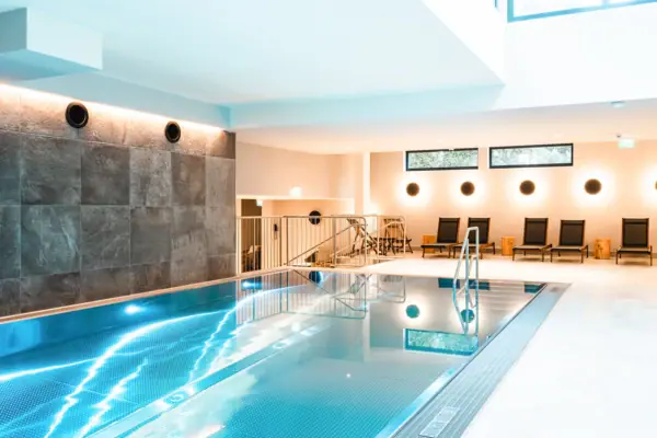 Indoor-Pool im HENRI Kitzbühel Ein Innenpool mit Treppe und Stühlen.
