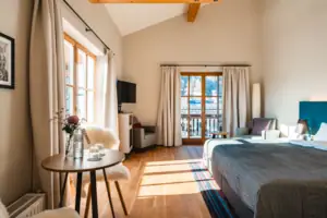 Geräumiges Zimmer mit Tisch und Doppelbett, lichtdurchfluetet mit vielen Fenstern.