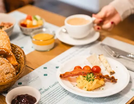 Frühstückstisch HENRI Hotel Eine Person hält eine Tasse Kaffee und einen Teller mit Essen.