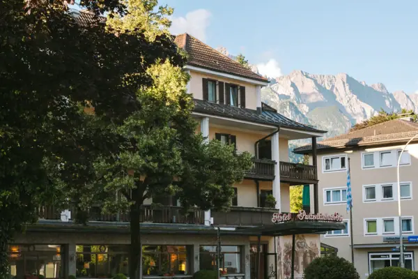HENRI Garmisch-Partenkirchen Außenansicht Ein Gebäude mit Bäumen und Bergen im Hintergrund.