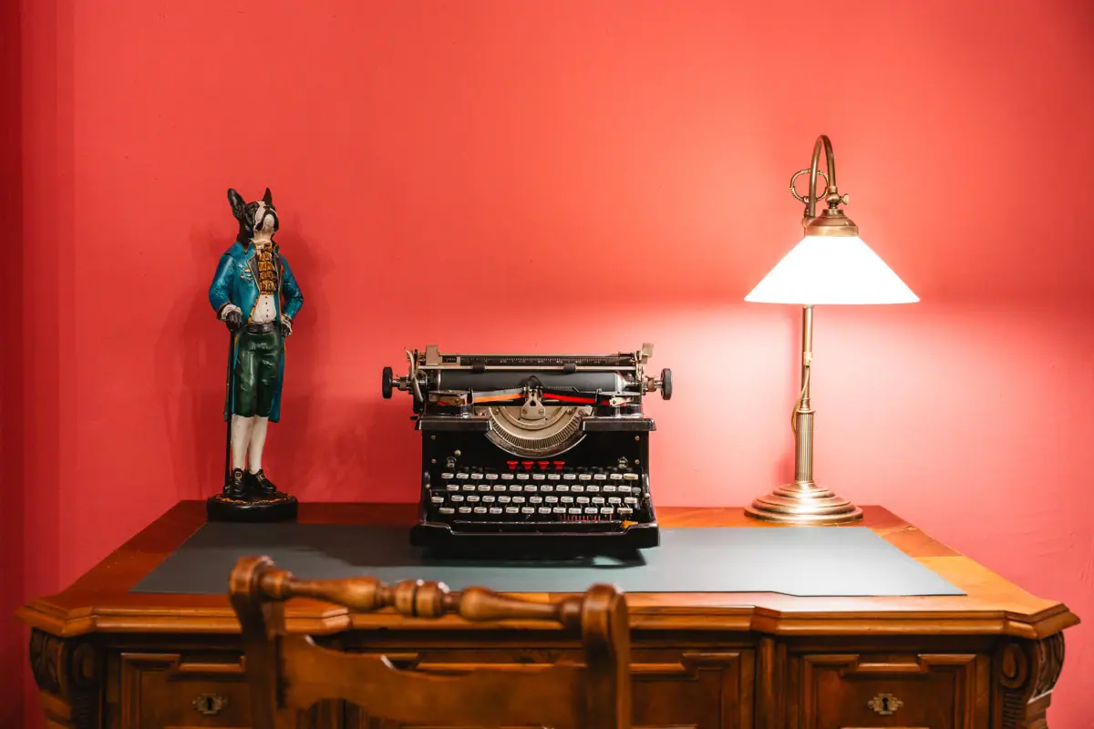 Roter Salon Ein Schreibtisch mit einer Lampe und einer Schreibmaschine.