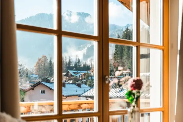 HENRI Kitzbühel Ein Fenster mit Blick auf eine Bergkette und eine Blumenvase auf einem Tisch.