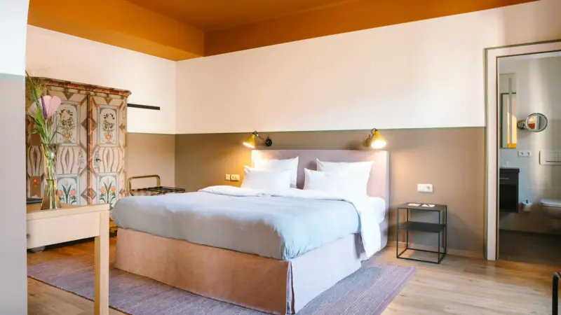 Zimmer im HENRI Hotel Garmisch-Partenkirchen Ein Hotelzimmer im HENRI Hotel Garmisch-Partenkirchen mit einem gemütlichen Bett und einem alten Schrank.