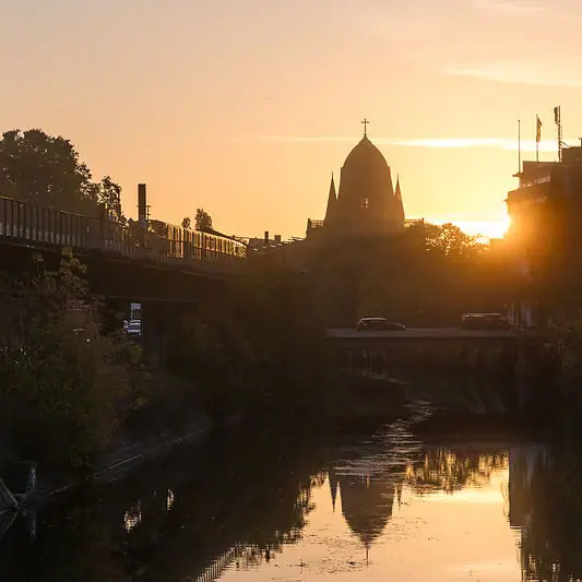 Brücke über einen Fluss mit einem Gebäude im Hintergrund bei Sonnenuntergang.