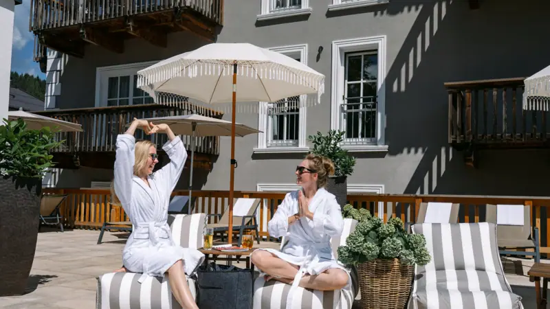 Sonnenterrasse im HENRI Hotel Kitzbühel Zwei Frauen in Bademänteln sitzen auf einer Terrasse.