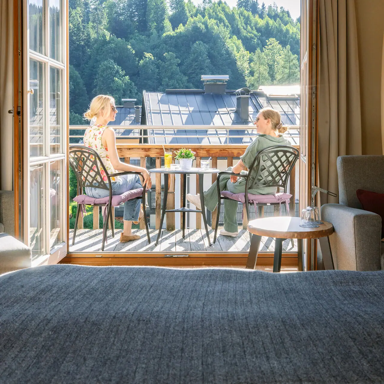Zwei Frauen sitzen auf einem Balkon und blicken aus einem Fenster.
