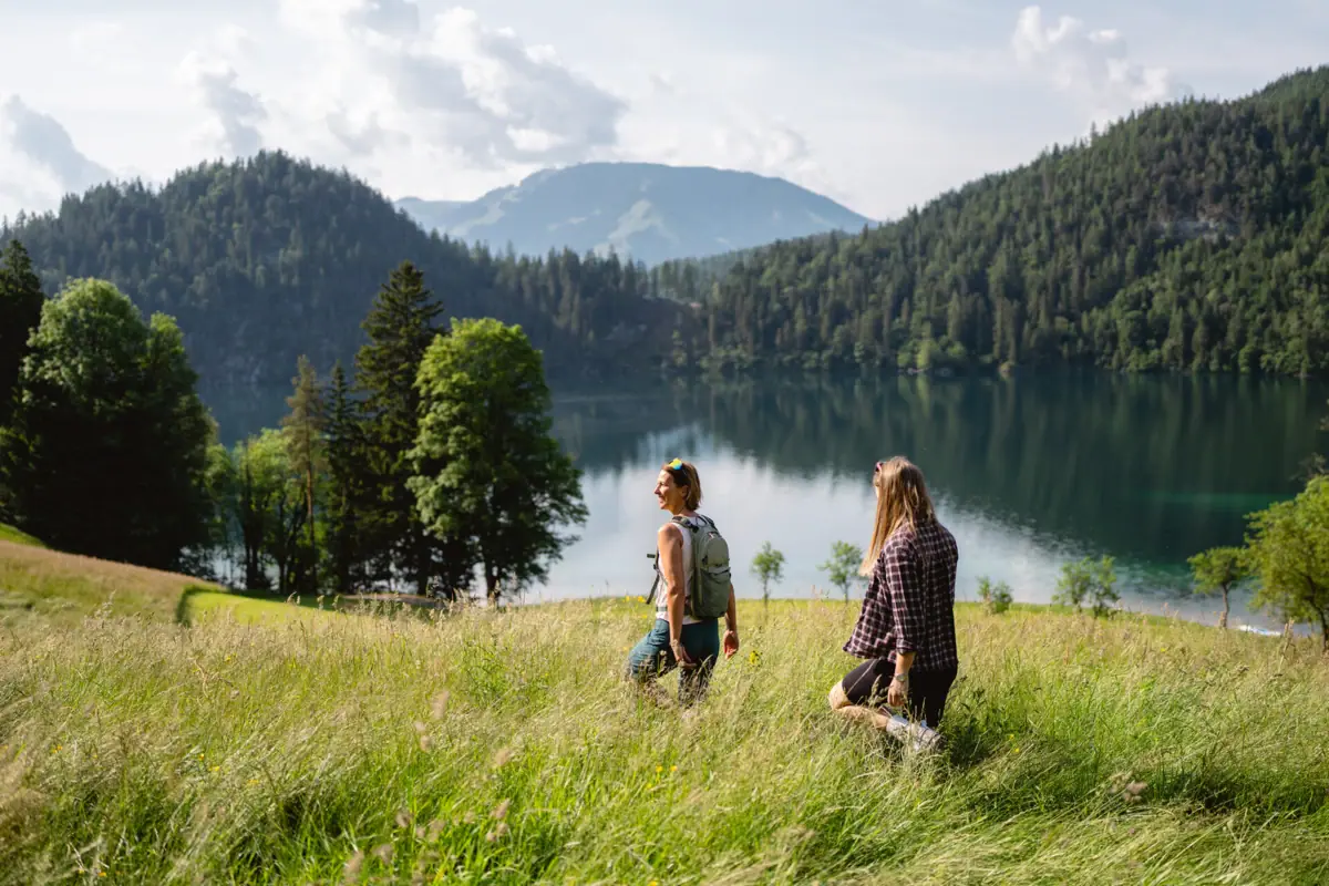 Zwei Personen stehen in einem grasbewachsenen Feld an einem See.