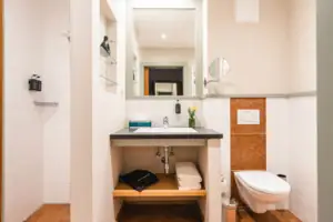 Badezimmer mit Waschbecken und Toilette, ausgestattet mit Spiegel und Armaturen.